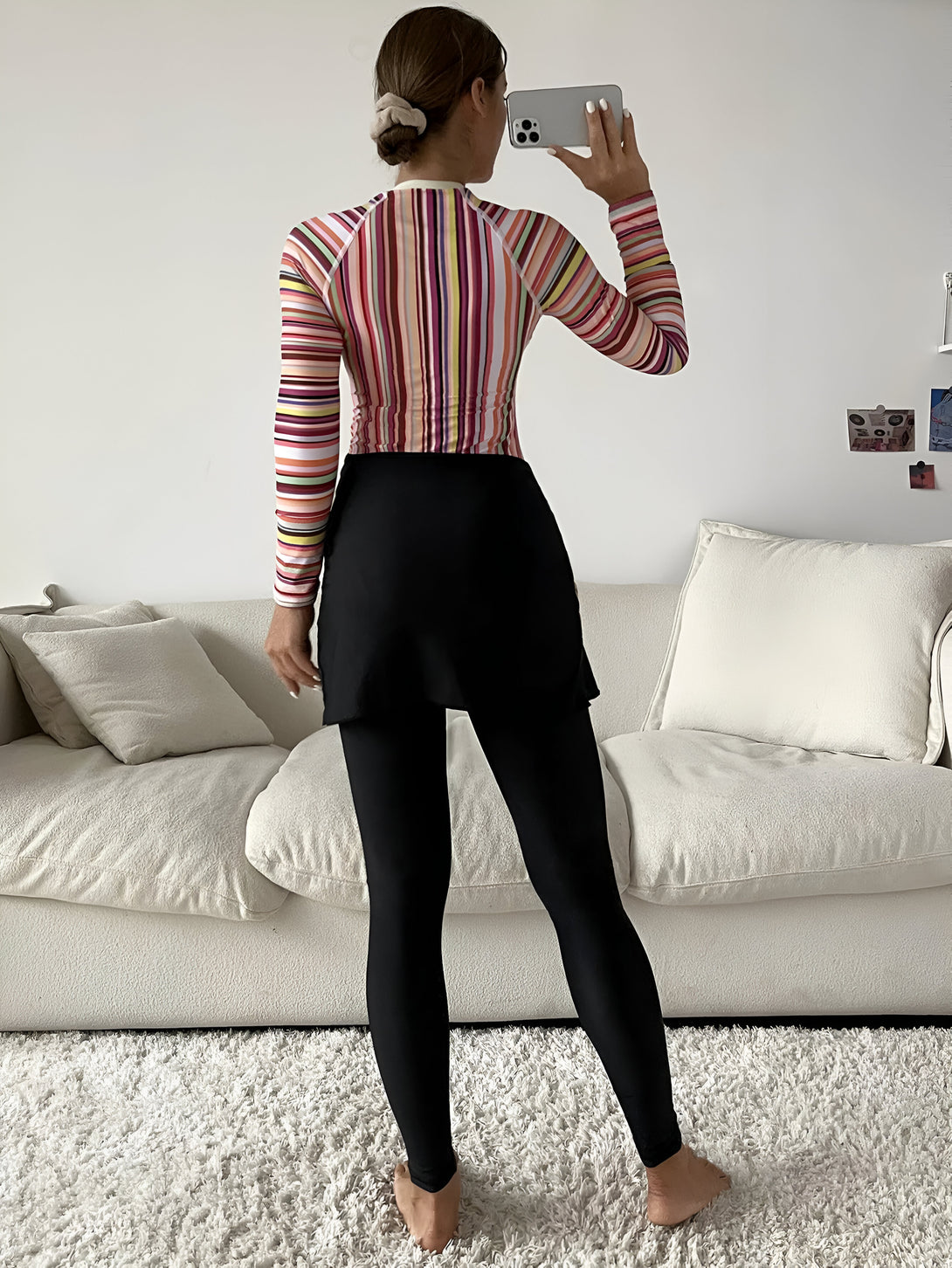 Une femme porte une tenue musulmane élégante avec un haut rayé coloré et un pantalon noir. La tenue est parfaite pour une occasion spéciale ou pour un usage quotidien.