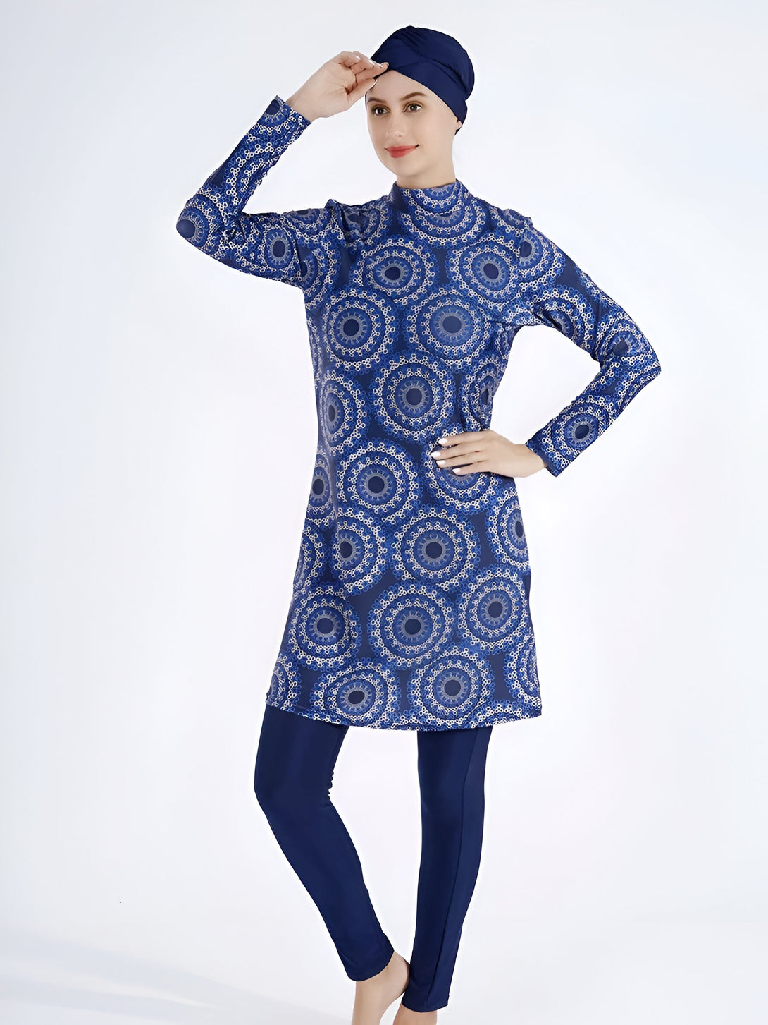 Une femme portant un maillot de bain musulman bleu avec un motif de mandalas blancs. Le maillot de bain comprend une tunique à manches longues et un pantalon long. Elle porte également un foulard bleu.