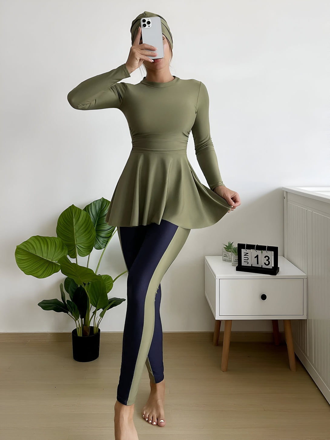 Une femme portant un hijab et un maillot de bain musulman vert et bleu à motifs. Elle se tient debout sur un sol en bois.
