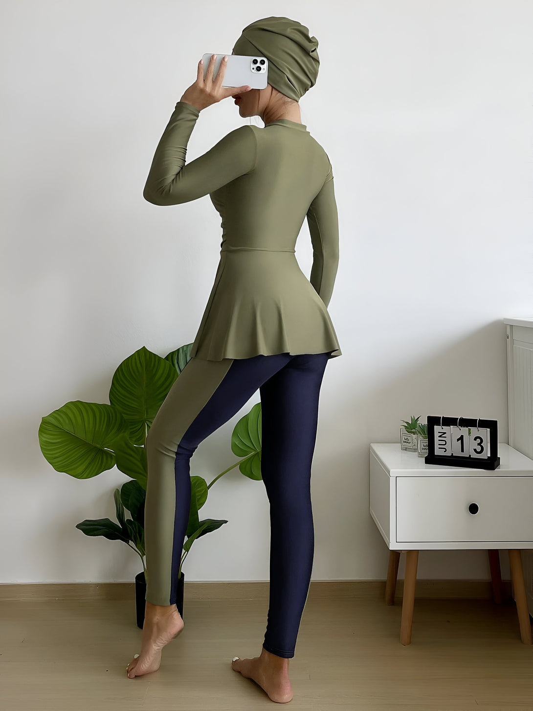 Une femme portant un hijab vert et un maillot de bain musulman vert et bleu.  Elle pose dans un intérieur moderne.