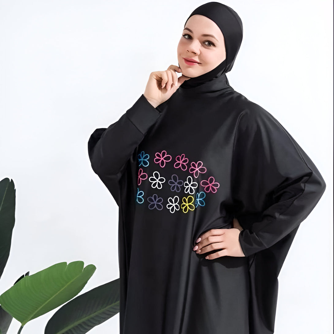 Une femme porte un maillot de bain musulman noir avec des fleurs colorées brodées sur la poitrine.