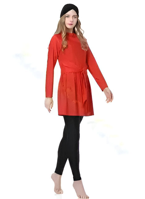 Une femme porte un maillot de bain musulman rouge avec un pantalon noir. Le maillot de bain est à manches longues et a une ceinture à la taille. La femme porte également un bandeau noir sur la tête.