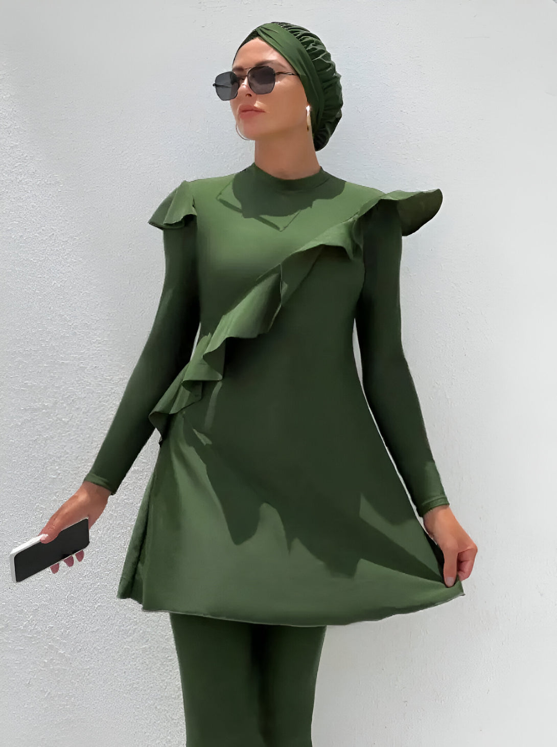 Une femme porte un maillot de bain musulman vert avec des volants. Elle porte également un hijab et des lunettes de soleil.