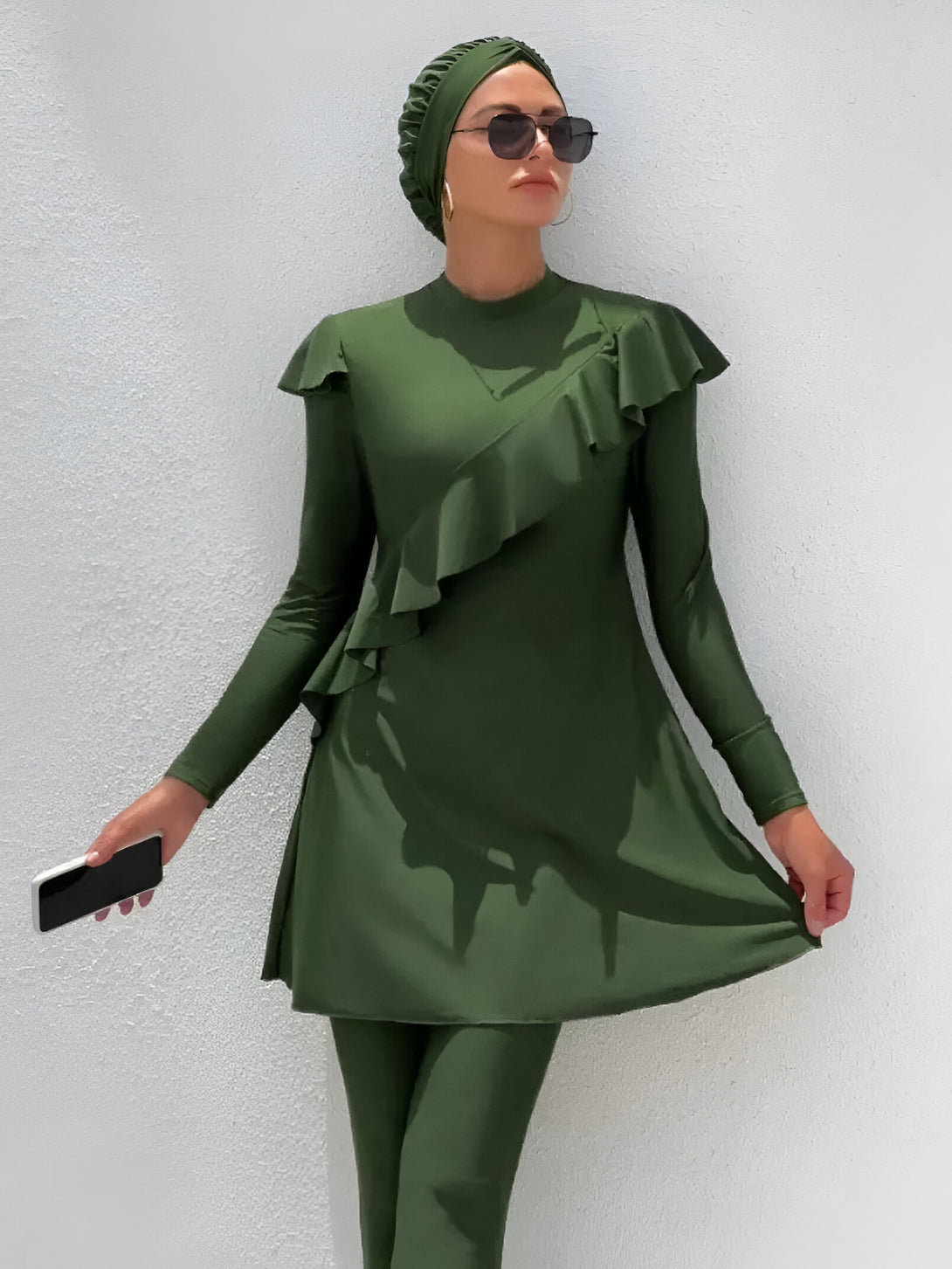 Une femme portant un maillot de bain musulman vert avec des volants. Elle porte également un foulard assorti et des lunettes de soleil.