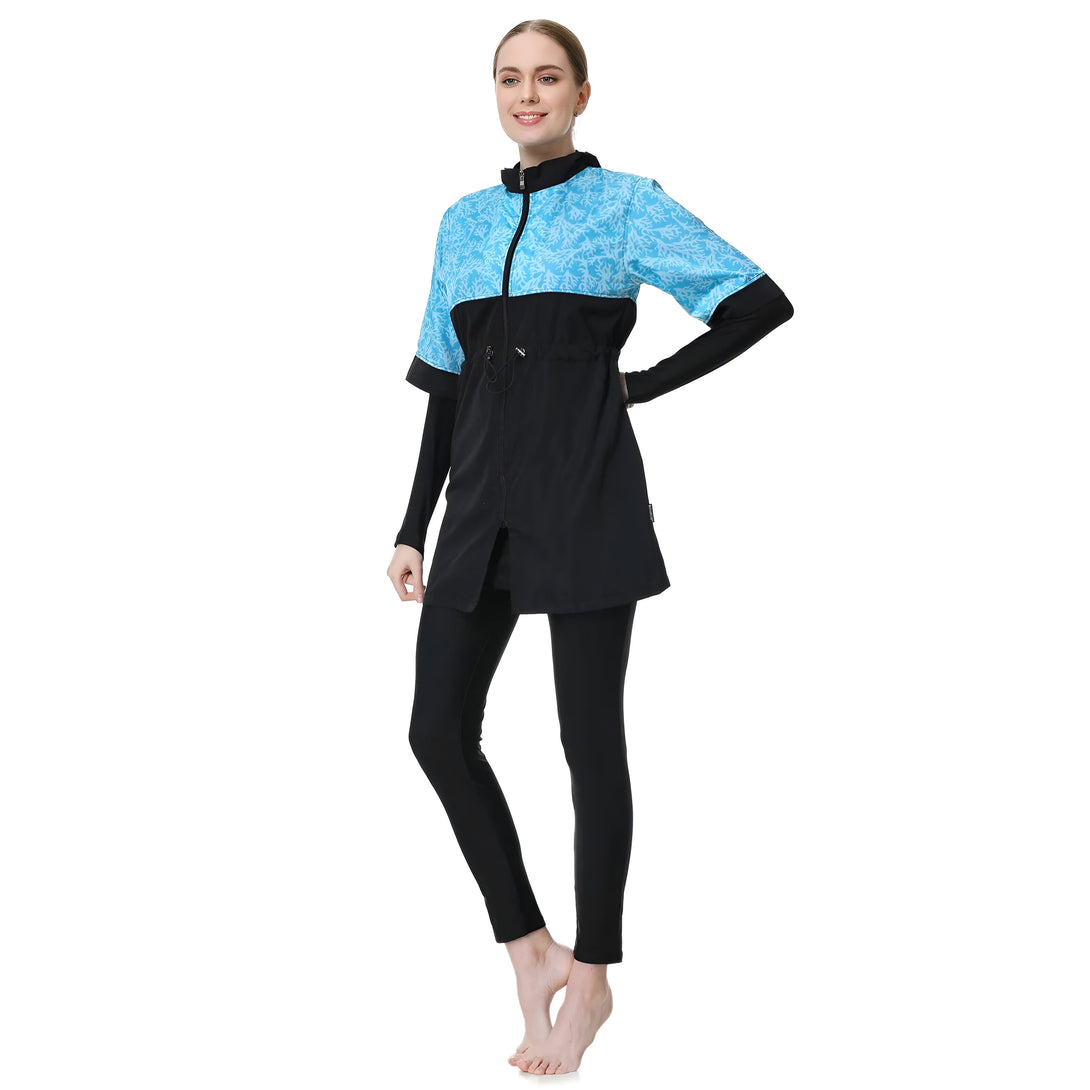 Une femme portant un maillot de bain musulman noir et bleu avec un motif de corail. Le maillot de bain comprend une chemise à manches longues avec une fermeture éclair et un pantalon long.