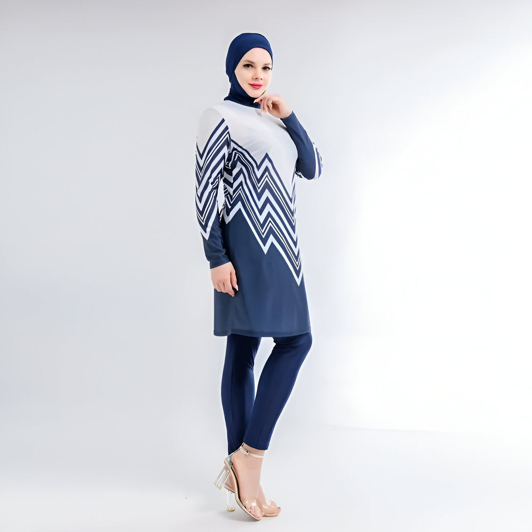 Une femme portant un maillot de bain musulman bleu et blanc avec un motif de chevrons. Le maillot de bain est à manches longues et comprend un pantalon long. La femme porte également un hijab bleu.