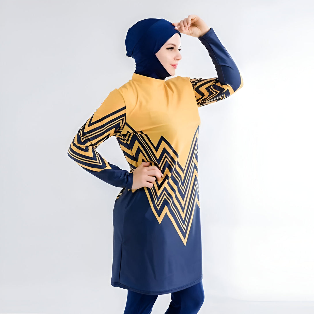 Une femme portant un maillot de bain musulman jaune et bleu avec un motif géométrique. Le maillot de bain est à manches longues et a une jupe longue. La femme porte également un hijab bleu foncé.