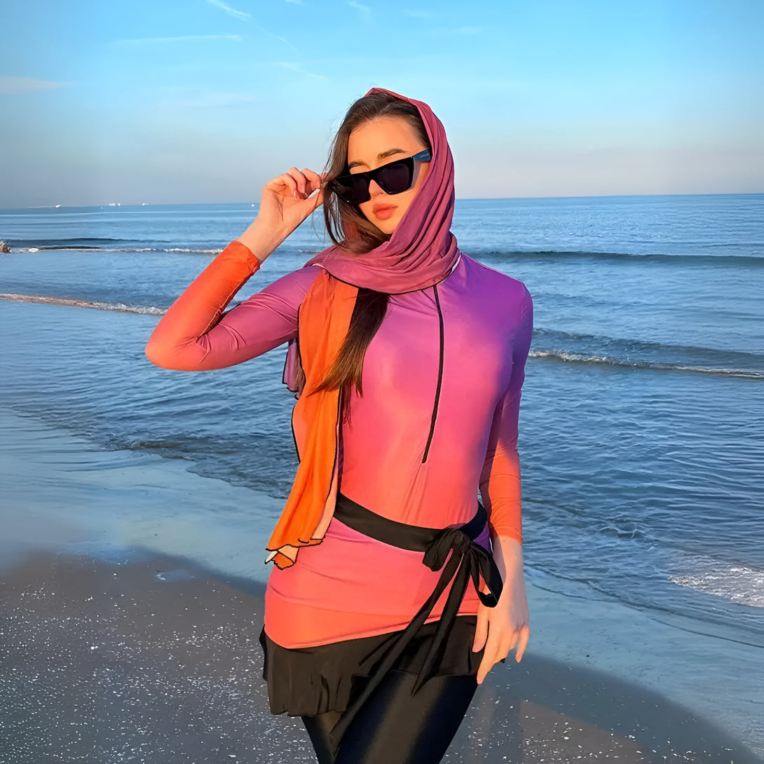 Une femme portant un hijab et un maillot de bain musulman rose et orange sur la plage.