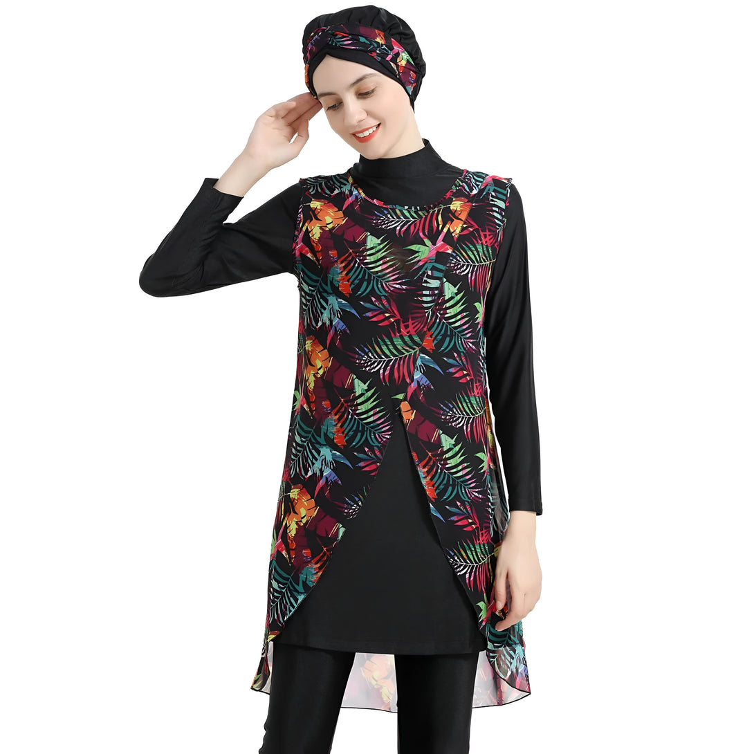 Une femme portant un hijab noir et une robe de bain musulmane à manches longues avec un motif tropical coloré. La robe de bain est noire et a une coupe longue avec un chemisier superposé à imprimé tropical.