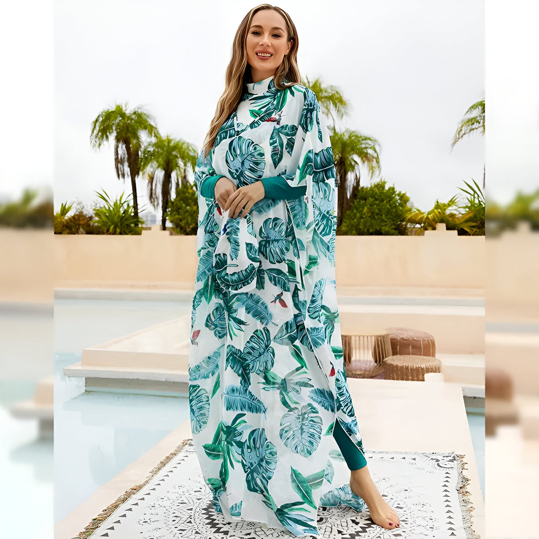 Une femme portant une robe de plage musulmane à imprimé tropical vert et blanc. La robe est longue et ample, avec des manches longues. La femme sourit à la caméra.