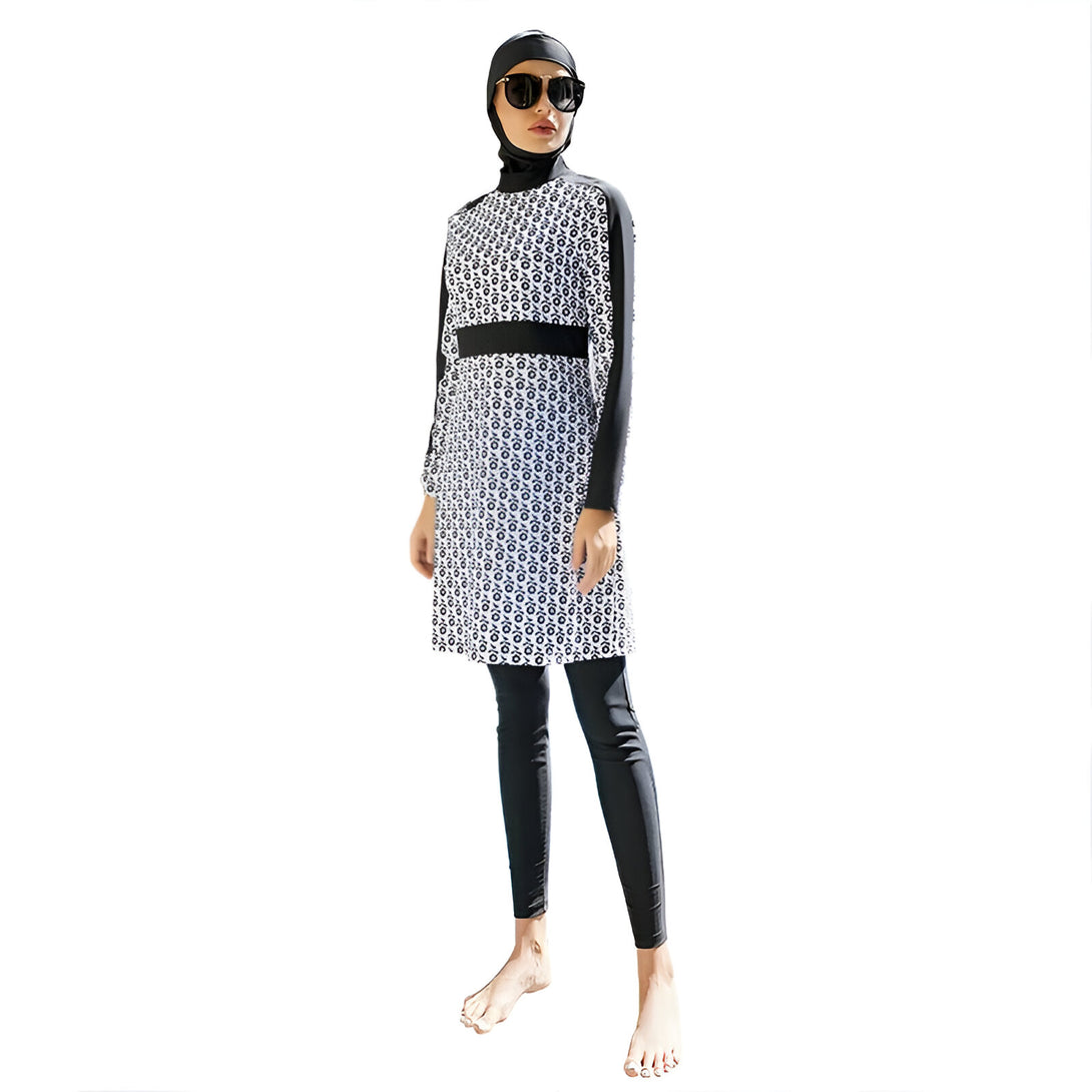 Une femme portant un maillot de bain musulman noir et blanc à motifs. Le maillot de bain est composé d'une robe longue et d'un pantalon. La femme porte un voile noir et des lunettes de soleil.