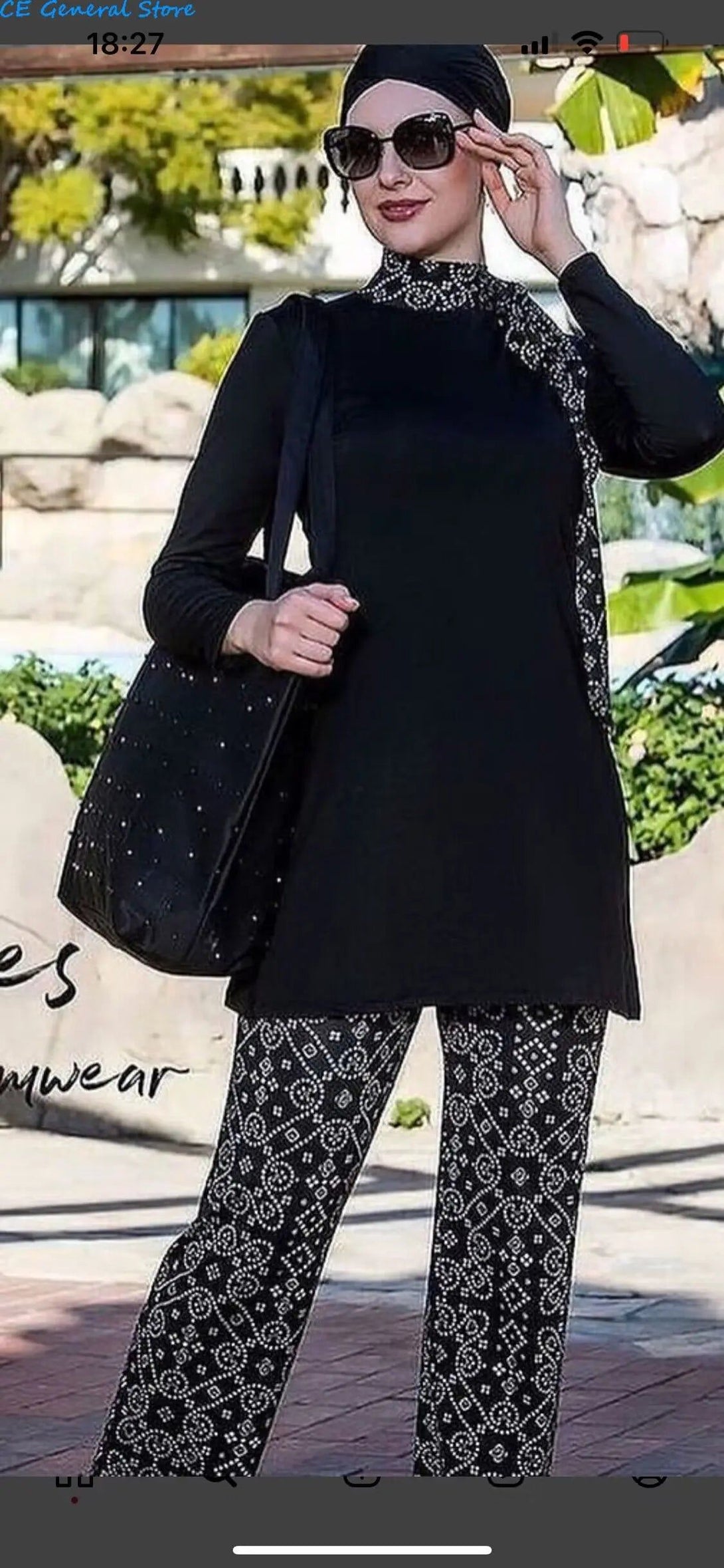 Une femme portant une tenue de bain noire à motif blanc et un hijab, avec un sac à main noir.