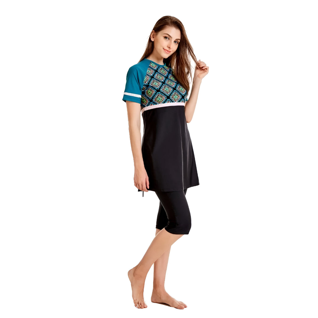 Une femme souriante portant un maillot de bain musulman noir et bleu avec un motif géométrique. Le maillot de bain est composé d'une tunique à manches courtes et d'un pantalon long.