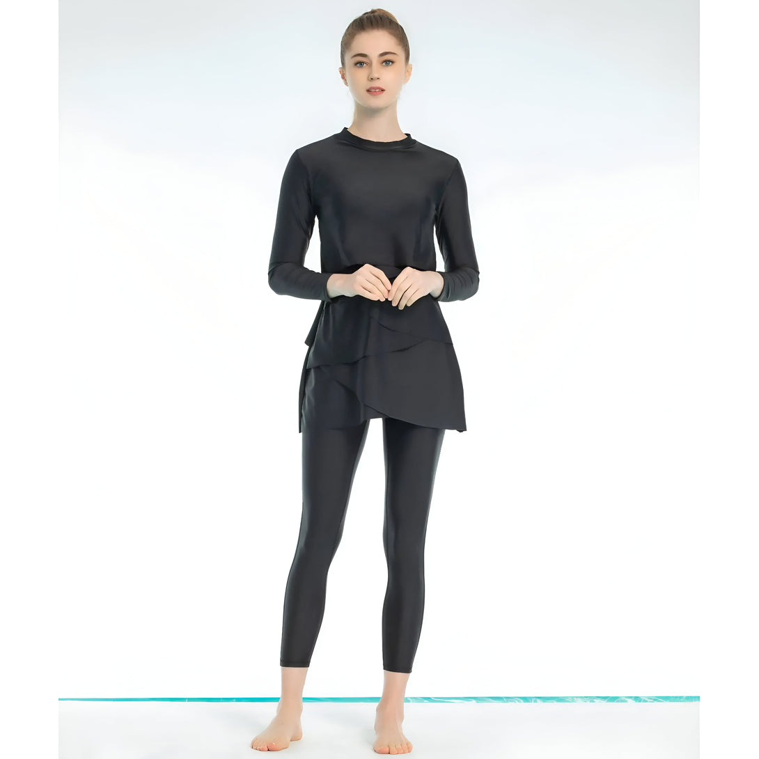 Une femme portant un maillot de bain musulman noir avec une jupe à volants et un pantalon long.  Le maillot de bain est parfait pour la natation et le bronzage tout en restant couvert.
