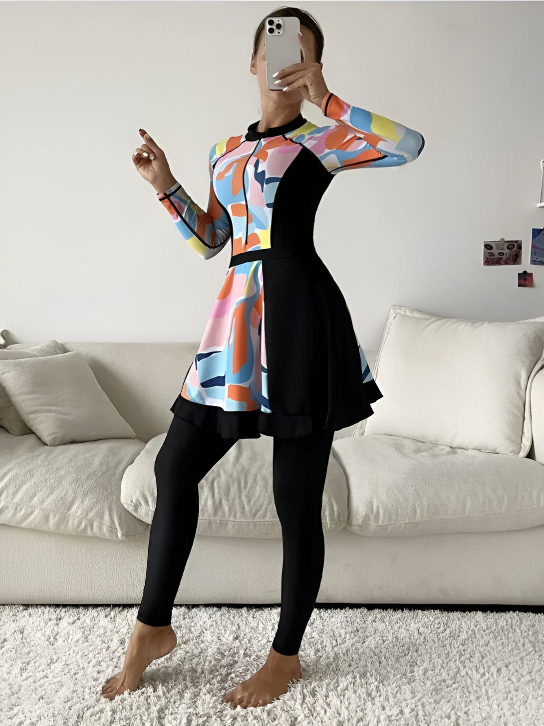 Une femme portant une robe de bain islamique avec des manches longues et une jupe, à motifs abstraits bleus, roses, jaunes et oranges. La robe est assortie d'un legging noir.