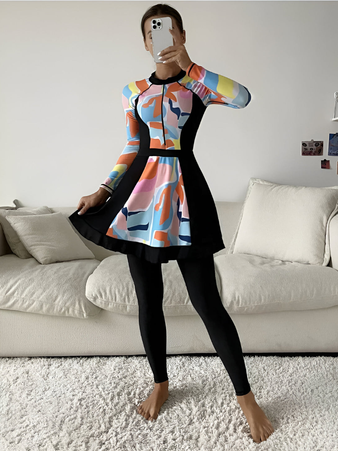 Une femme porte une robe longue de bain musulmane avec des manches longues et une jupe. La robe est de couleur noire et bleue avec des motifs abstraits colorés.