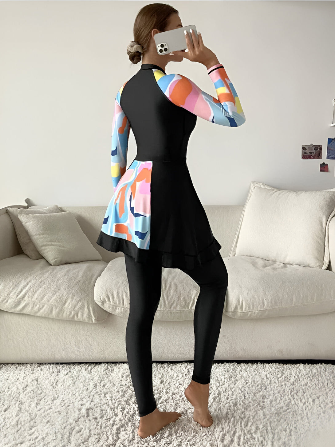 Une femme porte une robe de bain musulmane noire et colorée avec des manches longues et une jupe courte. La robe est ornée d'un motif abstrait et coloré.
