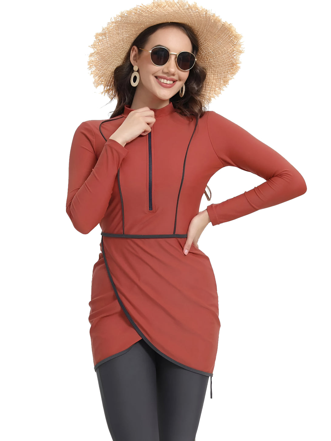 Une femme souriante portant un maillot de bain musulman rouge à manches longues avec une fermeture éclair sur le devant, un pantalon noir et un chapeau de paille.