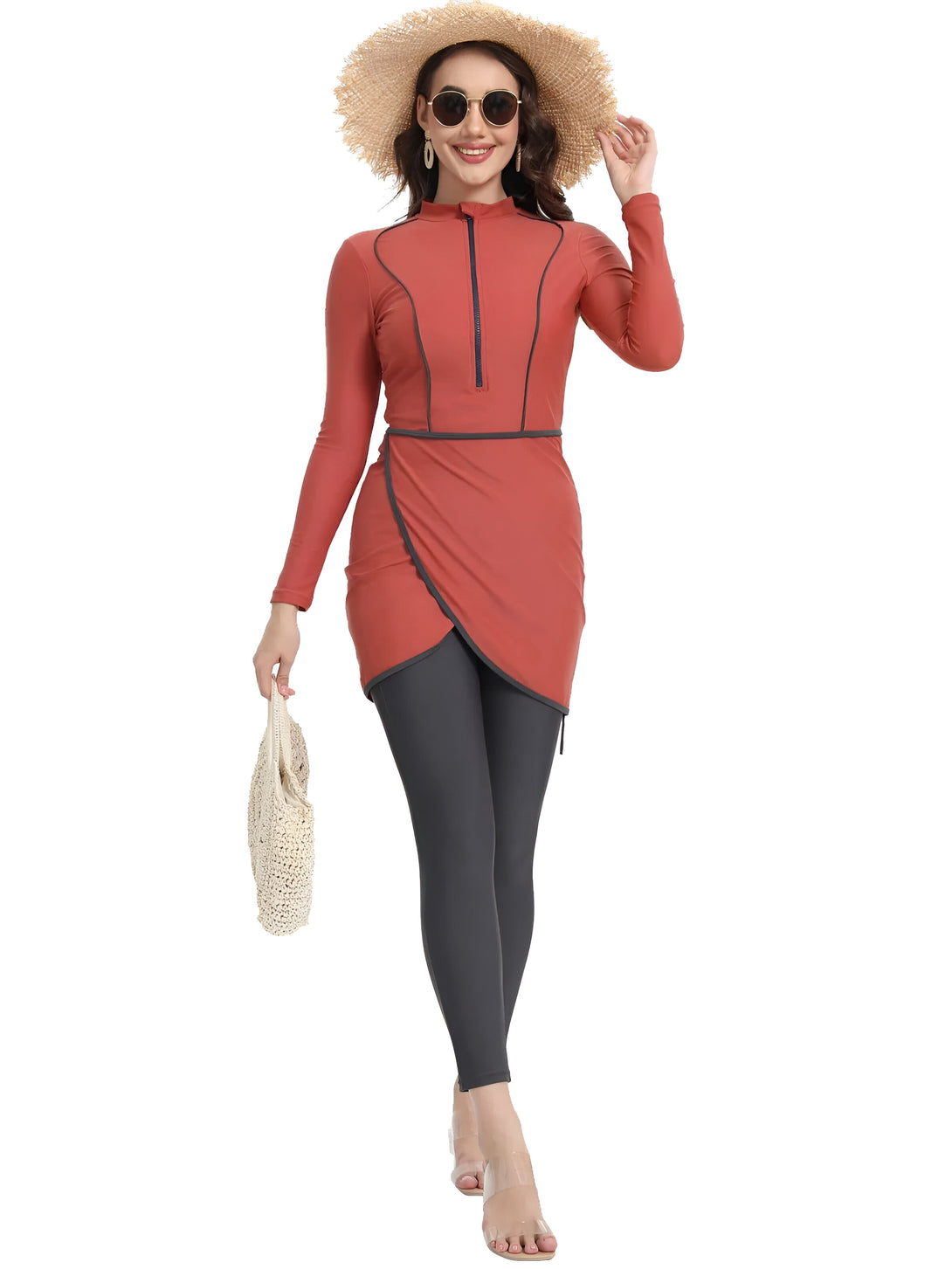 Une femme portant un maillot de bain musulman rouge avec une fermeture éclair et un pantalon noir, tenant un sac à main en paille et portant un chapeau de paille.