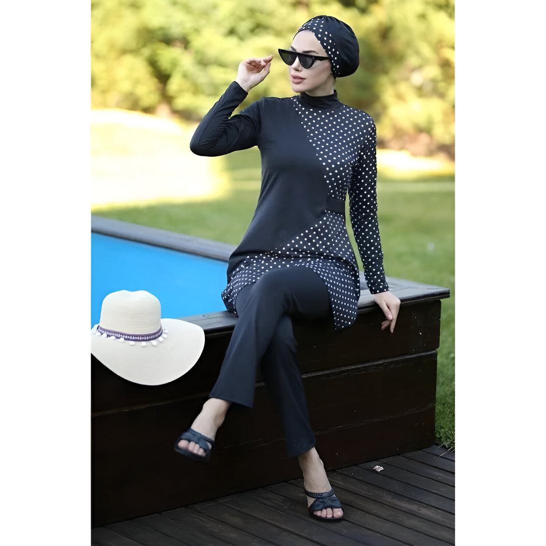 Une femme portant un maillot de bain musulman noir à pois blancs, assis près d'une piscine. Elle porte un hijab et des lunettes de soleil.