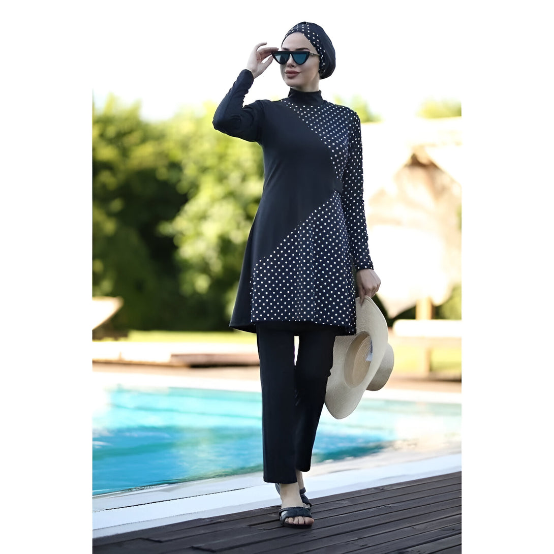 Une femme portant un maillot de bain musulman noir à pois blancs, une écharpe et des lunettes de soleil, debout près d'une piscine.