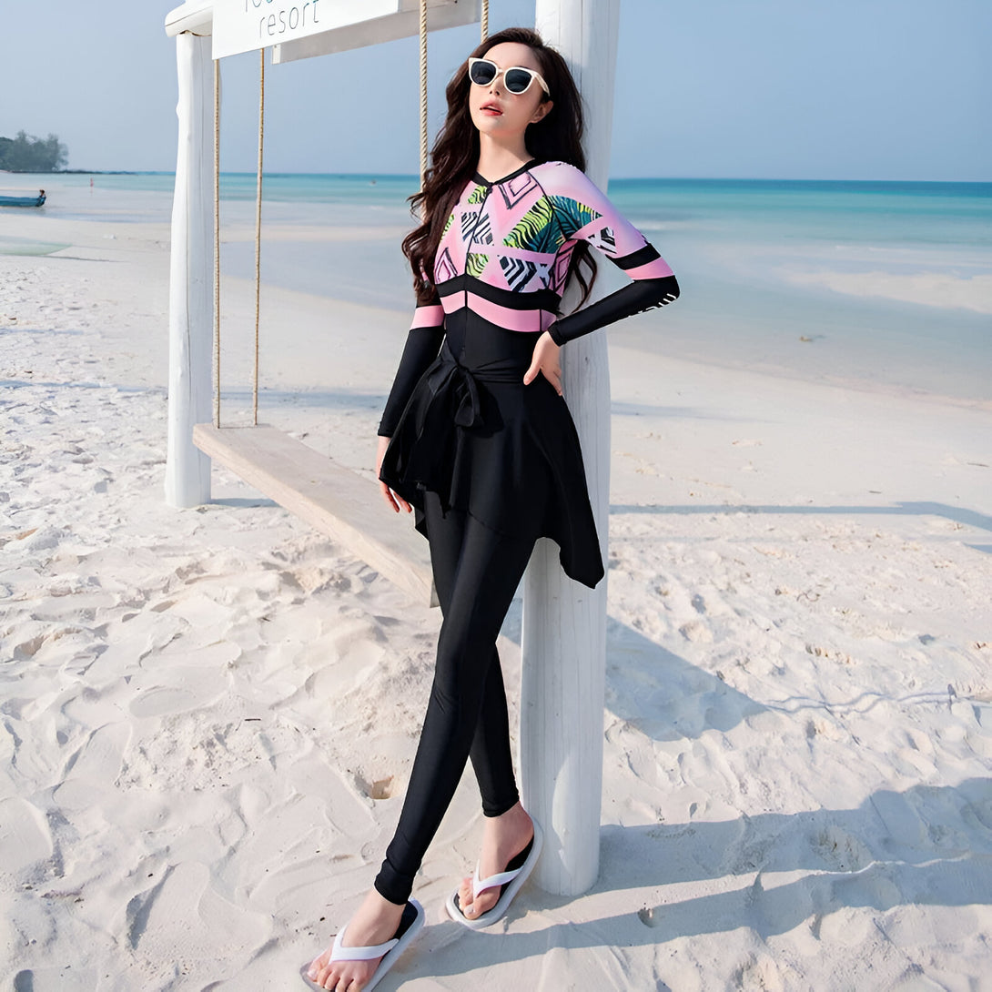 Une femme portant un maillot de bain musulman noir et rose avec des motifs tropicaux sur la plage.