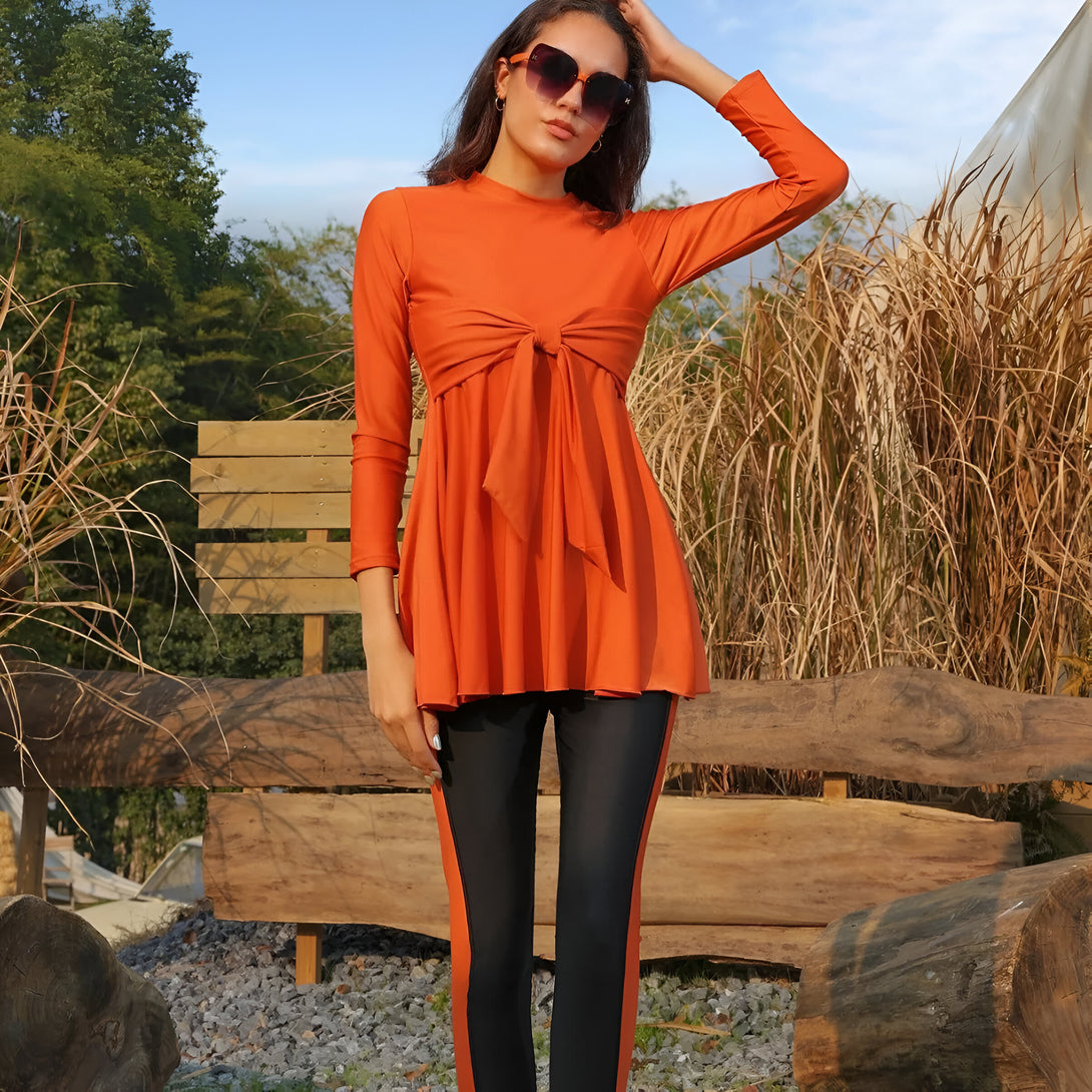 Une femme portant un ensemble de vêtements de bain musulmans orange et noirs, avec un nœud sur la poitrine. Elle porte également des lunettes de soleil.