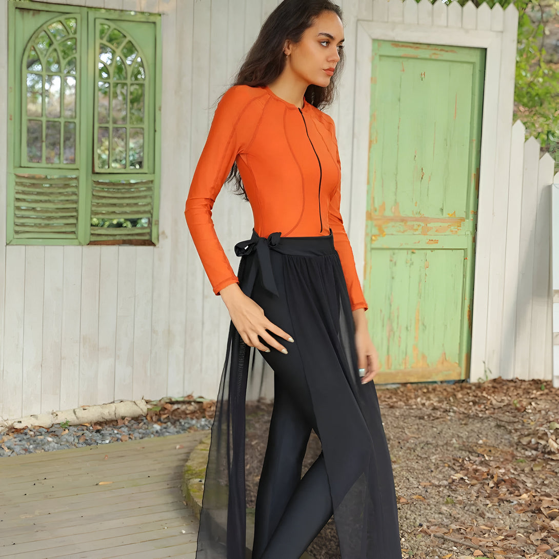 Une femme porte une robe de bain musulmane orange à manches longues avec une jupe noire en tulle.