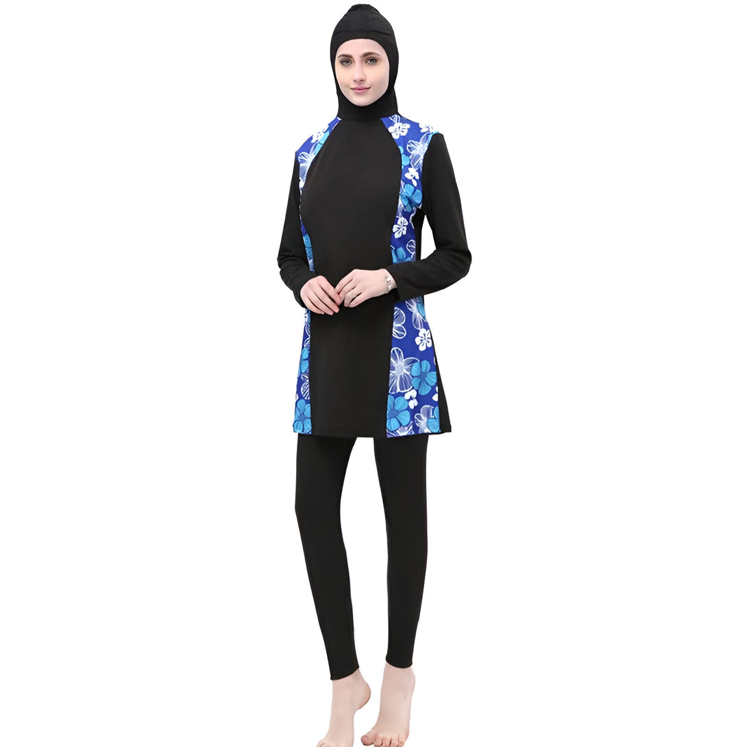 Une femme porte un maillot de bain musulman noir avec des détails floraux bleus. Le maillot de bain comprend une tunique à manches longues, un pantalon long et un hijab assorti.