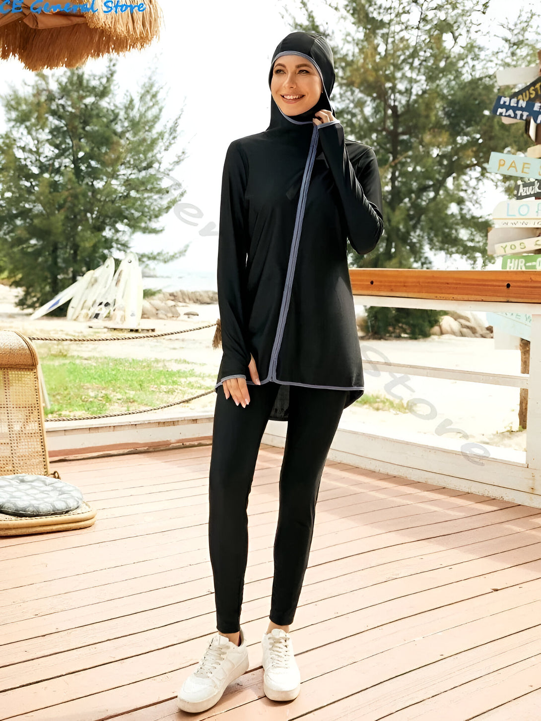 Une femme portant un hijab noir et un maillot de bain musulman noir avec des détails gris à l'extérieur d'un restaurant de plage.