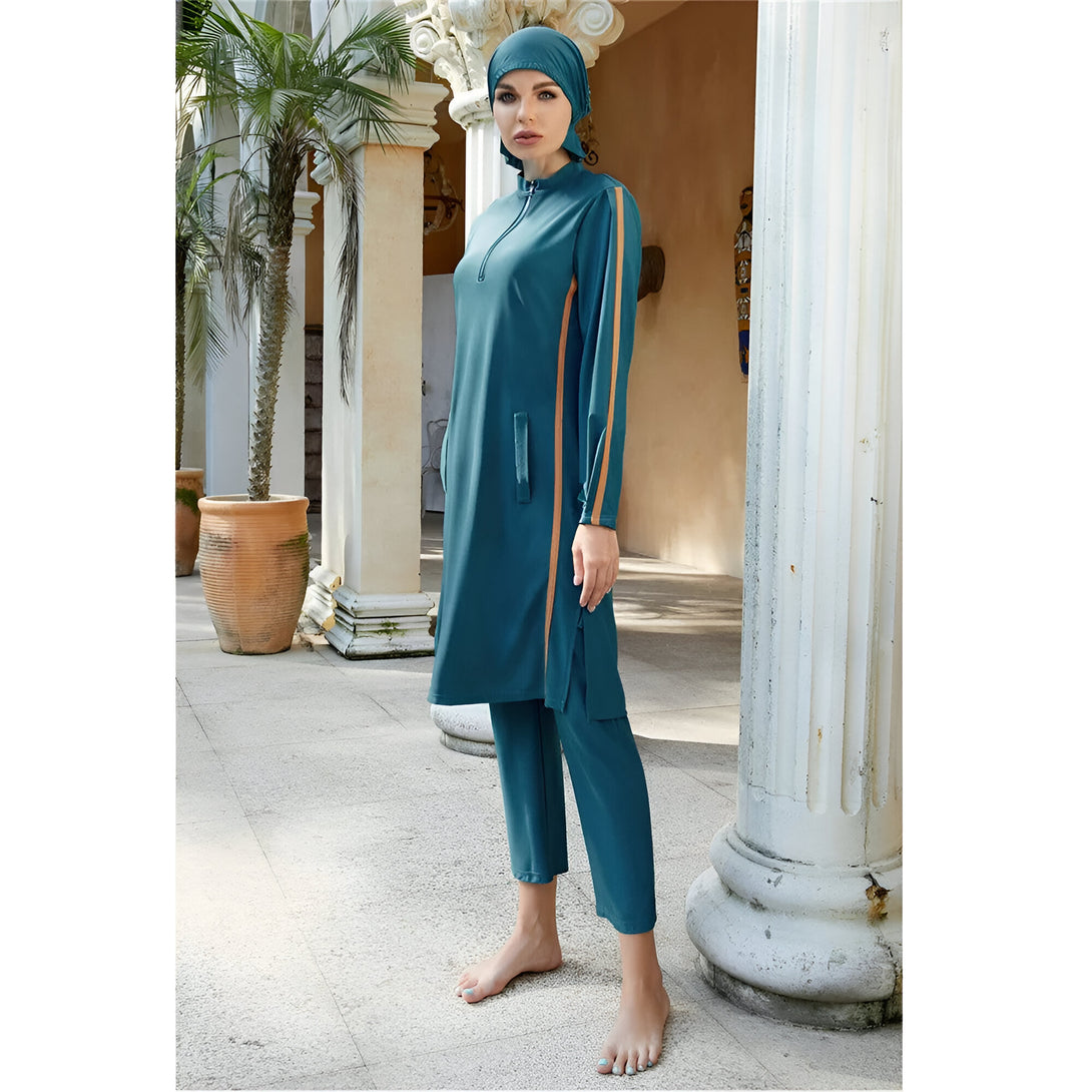 Une femme portant un maillot de bain musulman vert avec des détails orange. Le maillot de bain comprend une tunique à manches longues et un pantalon long. La femme porte également un hijab vert.