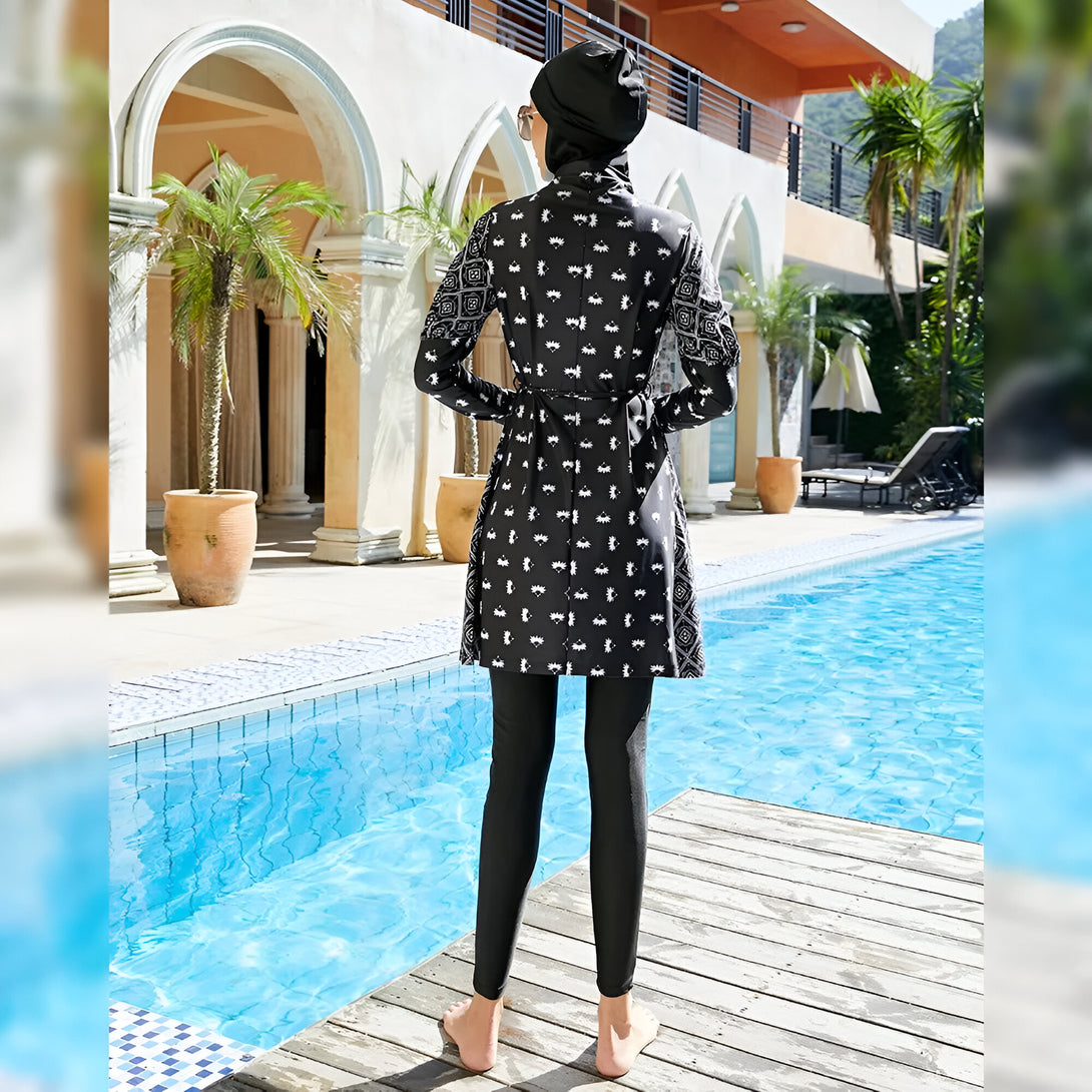 Une femme portant un maillot de bain musulman noir et blanc avec un motif géométrique se tient près d'une piscine.