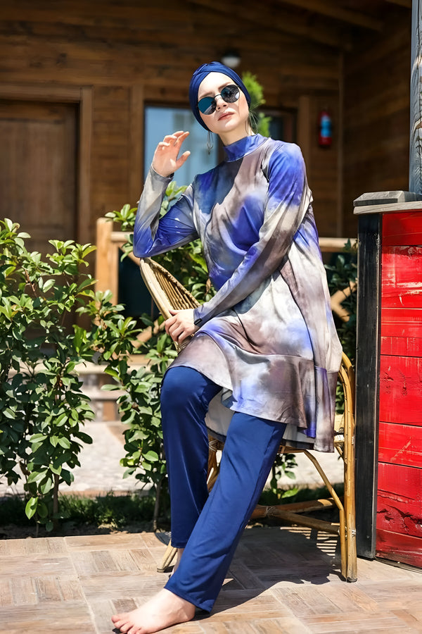 Une femme portant un hijab bleu et une robe de bain musulmane à imprimé bleu et gris, posant sur une chaise en rotin.
