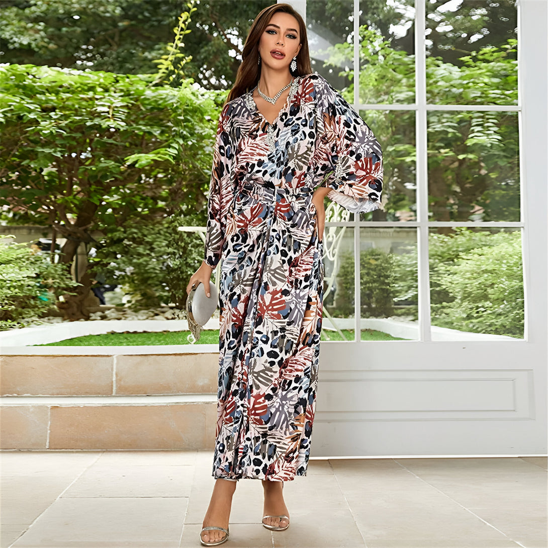 Une femme élégante porte une longue robe à manches longues avec un imprimé floral coloré. La robe est cintrée à la taille et a une encolure en V.  La femme porte des talons hauts et une pochette.