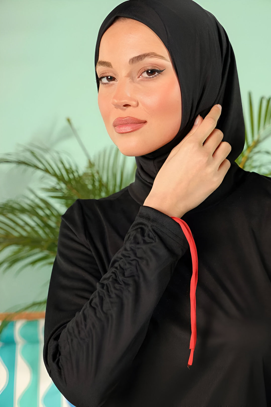 Une femme portant un hijab noir et une tenue de bain islamique noire avec des détails rouges.