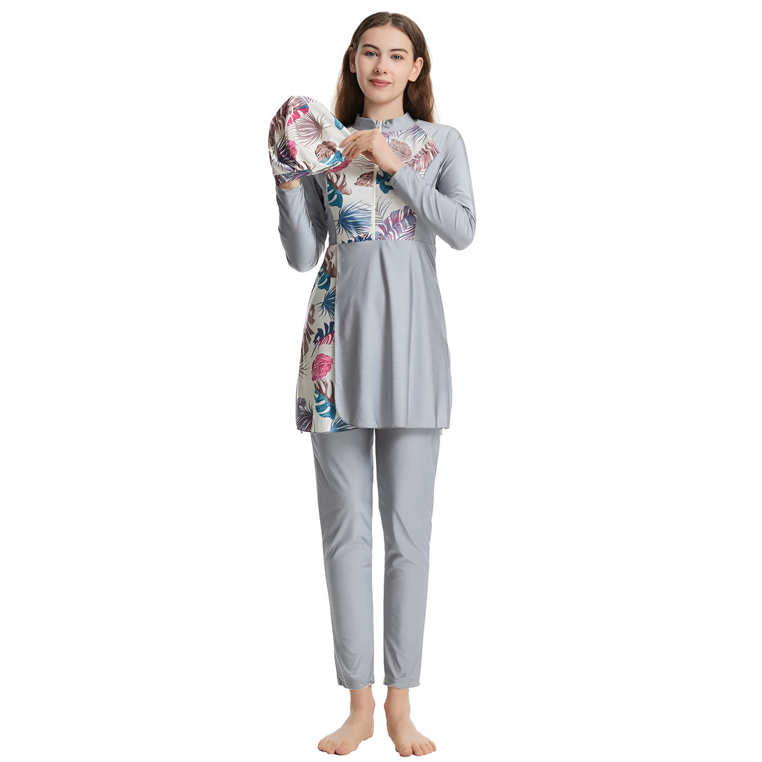 Une femme portant un maillot de bain musulman gris avec des motifs floraux. Le maillot de bain est composé d'une tunique à manches longues et d'un pantalon long. La femme porte également un bonnet de bain assorti.