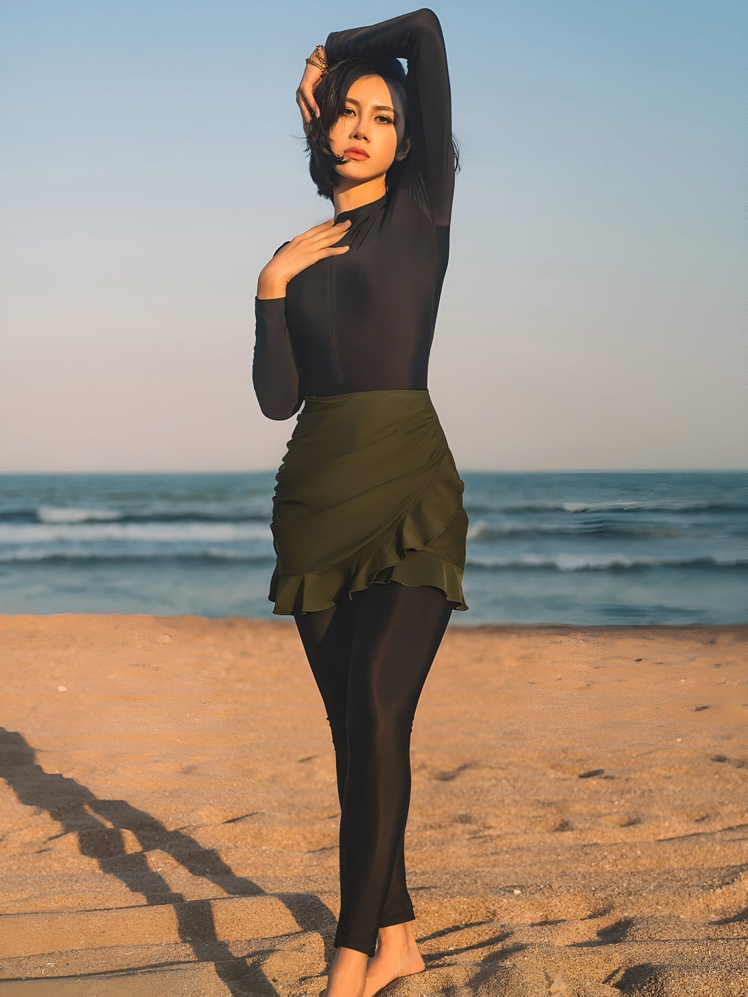 Une femme portant une tenue de bain islamique noire avec une jupe verte sur la plage.