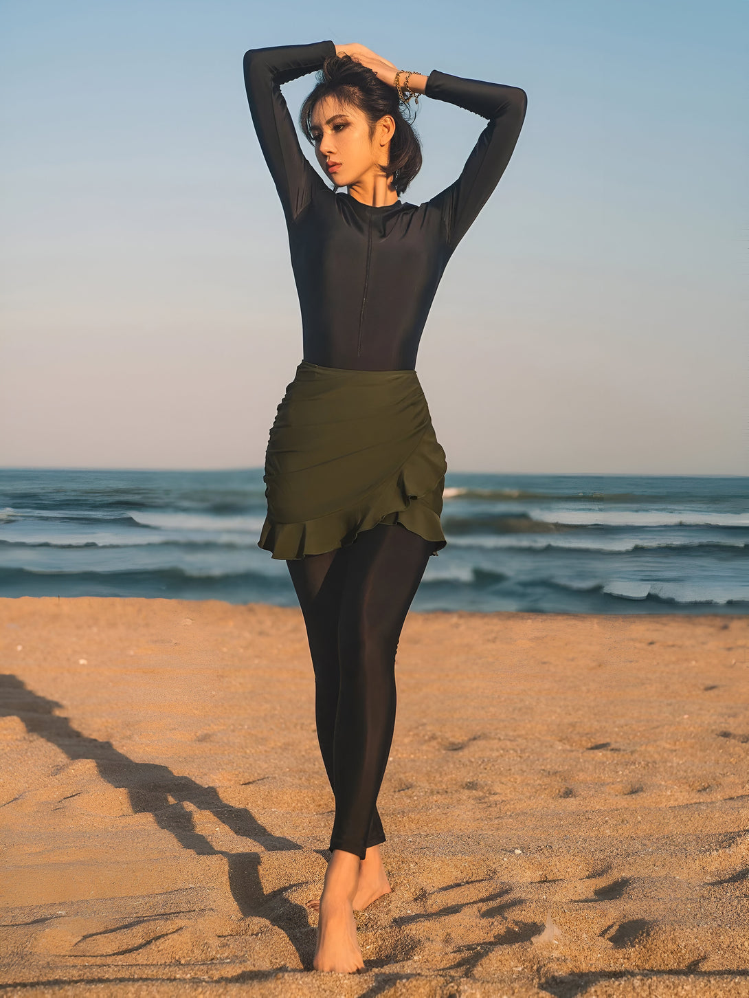 Une femme portant une tenue de plage musulmane noire et une jupe verte à volants se promène sur la plage.