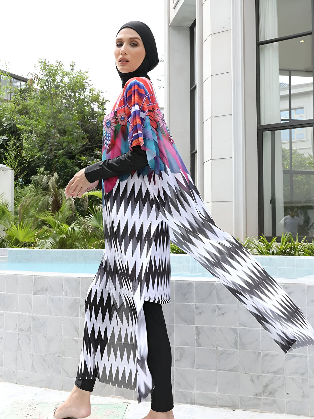 Une femme portant un maillot de bain musulman avec une robe longue à motifs géométriques noirs et blancs. Le maillot de bain est à manches longues et a un motif floral coloré.