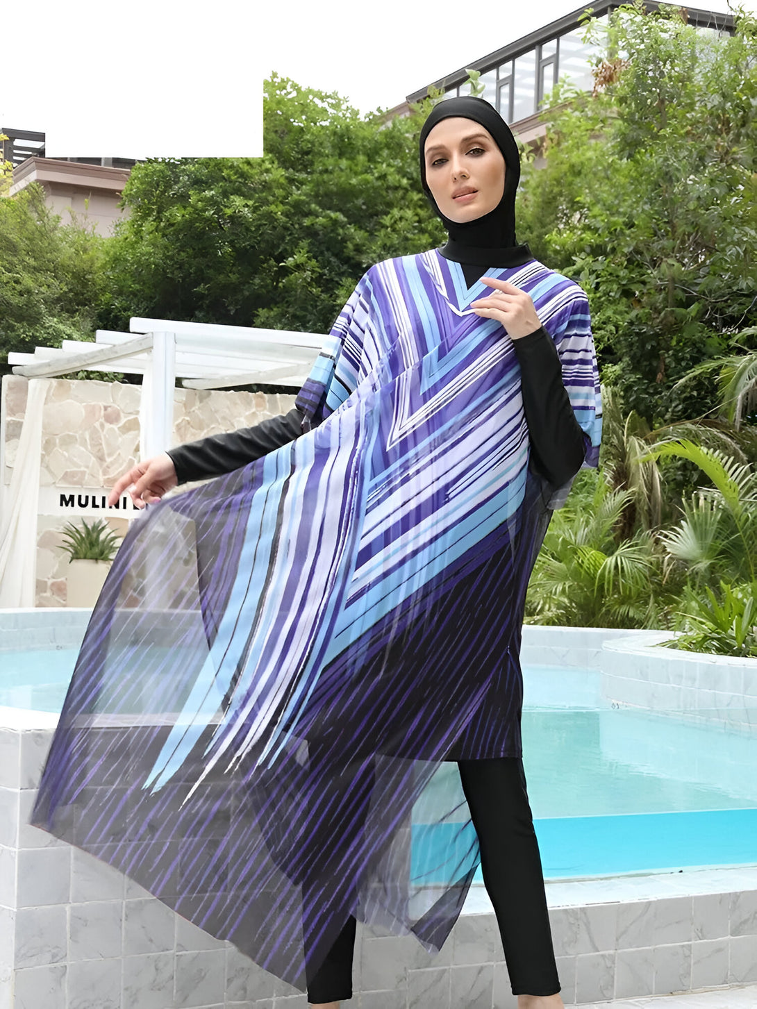 Une femme portant un maillot de bain musulman bleu et noir avec un hijab noir, debout près d'une piscine.