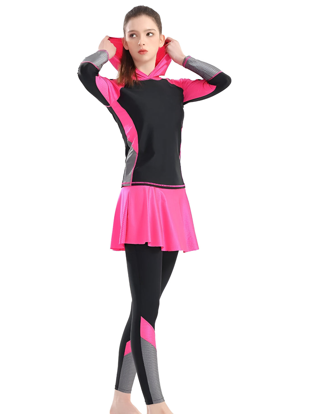 Une femme portant un ensemble de vêtements musulmans composé d'un haut à manches longues avec une capuche, une jupe et un legging. Le haut est noir avec des accents roses et gris, la jupe est rose et le legging est noir avec des accents roses et gris.