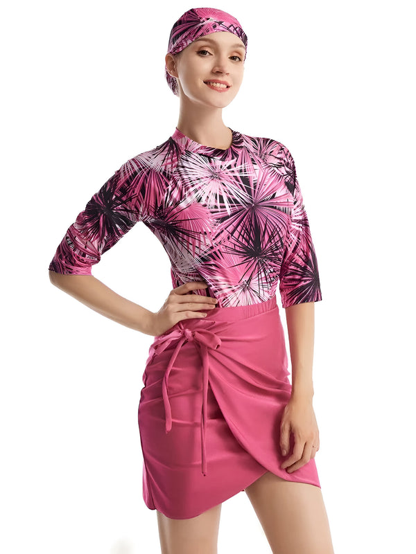 Une femme portant un hijab rose et une robe rose à imprimé tropical. La robe a des manches trois quarts et une jupe enveloppante.