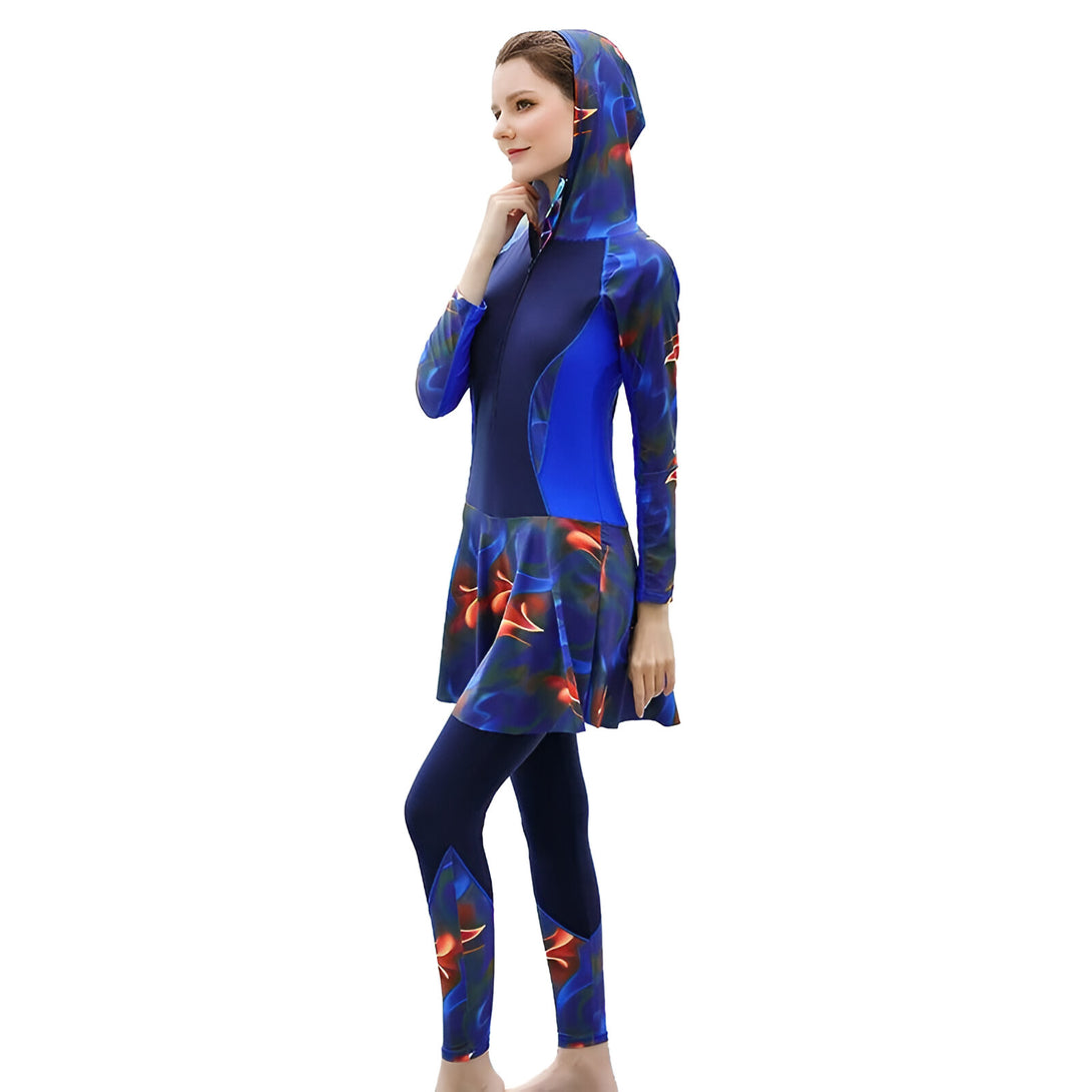 Une femme portant un maillot de bain musulman bleu et noir à motifs floraux. Le maillot de bain comprend une robe longue à manches longues avec une capuche et un pantalon ajusté.