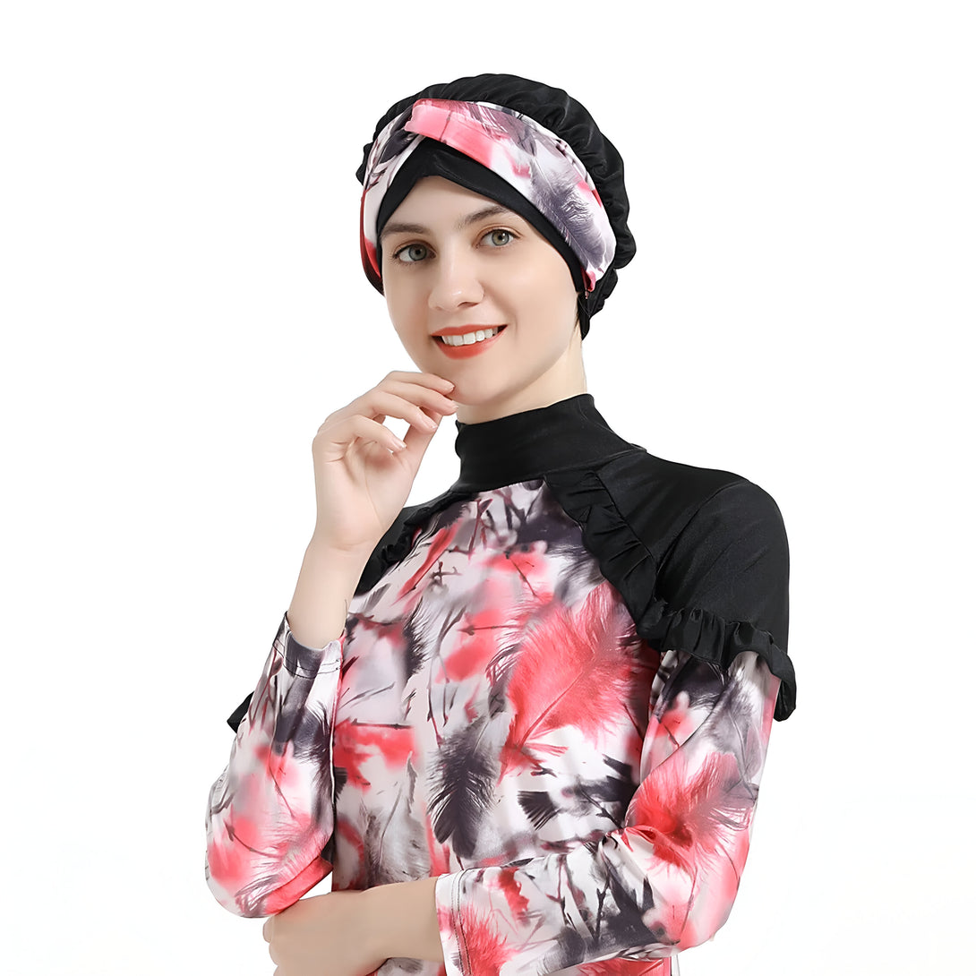 Une femme souriante porte un maillot de bain musulman à manches longues avec un motif de plumes rouges, noires et blanches. Elle porte également un turban noir avec un motif floral.