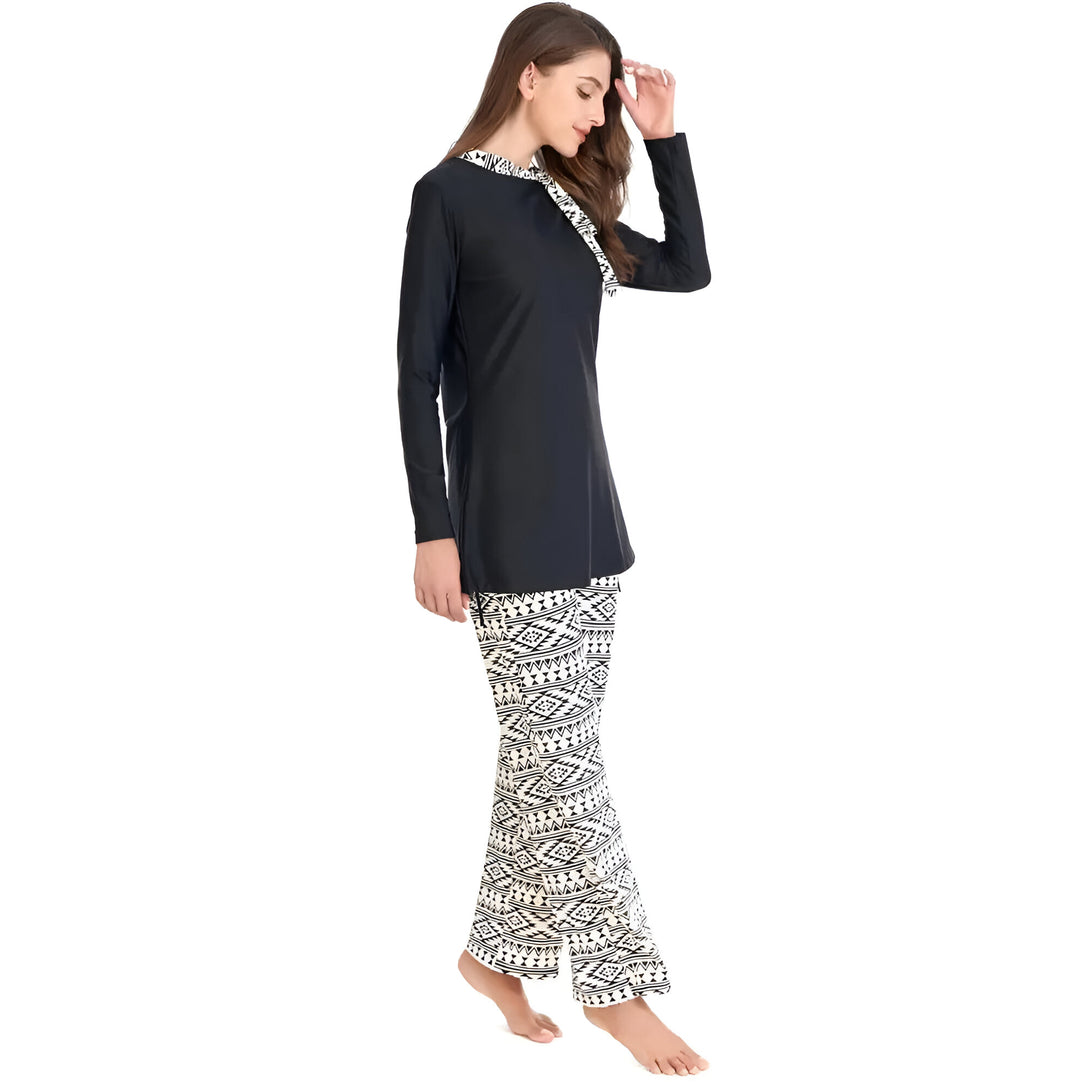 Une femme portant un maillot de bain musulman noir à manches longues avec un pantalon blanc à motifs géométriques noirs.