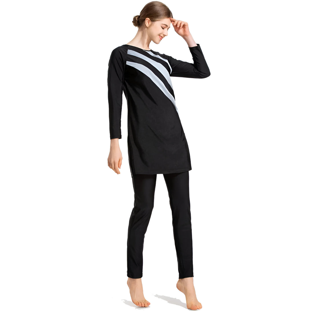 Une femme portant un maillot de bain musulman noir avec des rayures blanches. Le maillot de bain est à manches longues et couvre les jambes. La femme sourit et regarde vers le bas.