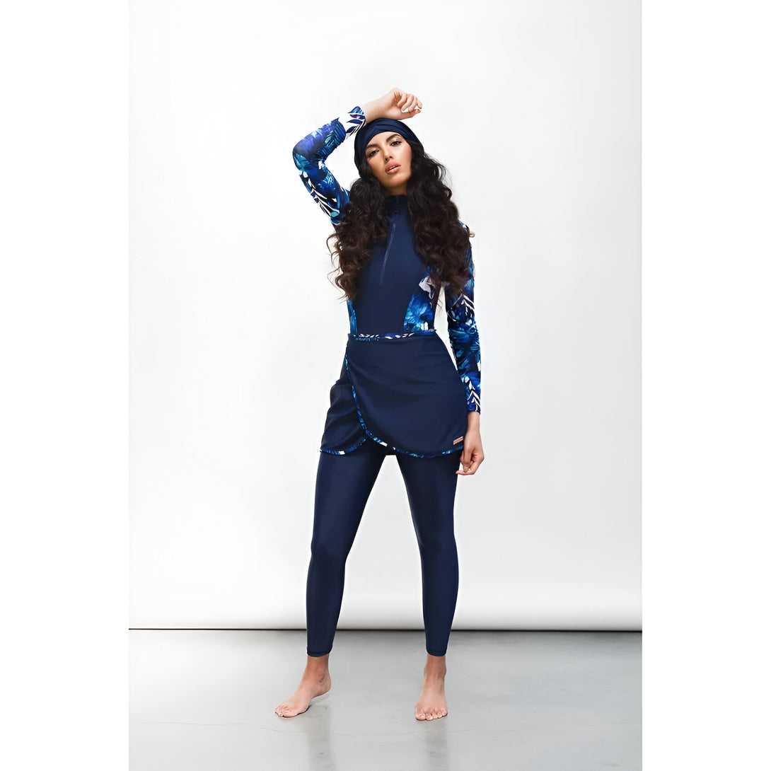 Une femme portant un maillot de bain musulman bleu marine avec un motif floral. Le maillot de bain comprend un haut à manches longues, un pantalon et une jupe. La femme porte un bonnet assorti.