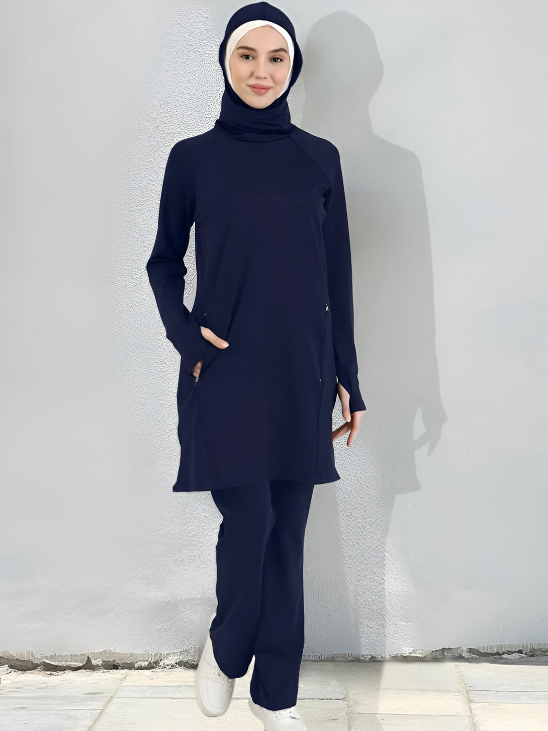 Une femme portant un ensemble de vêtements musulmans bleu marine, comprenant un haut à manches longues avec une capuche et un pantalon assorti.