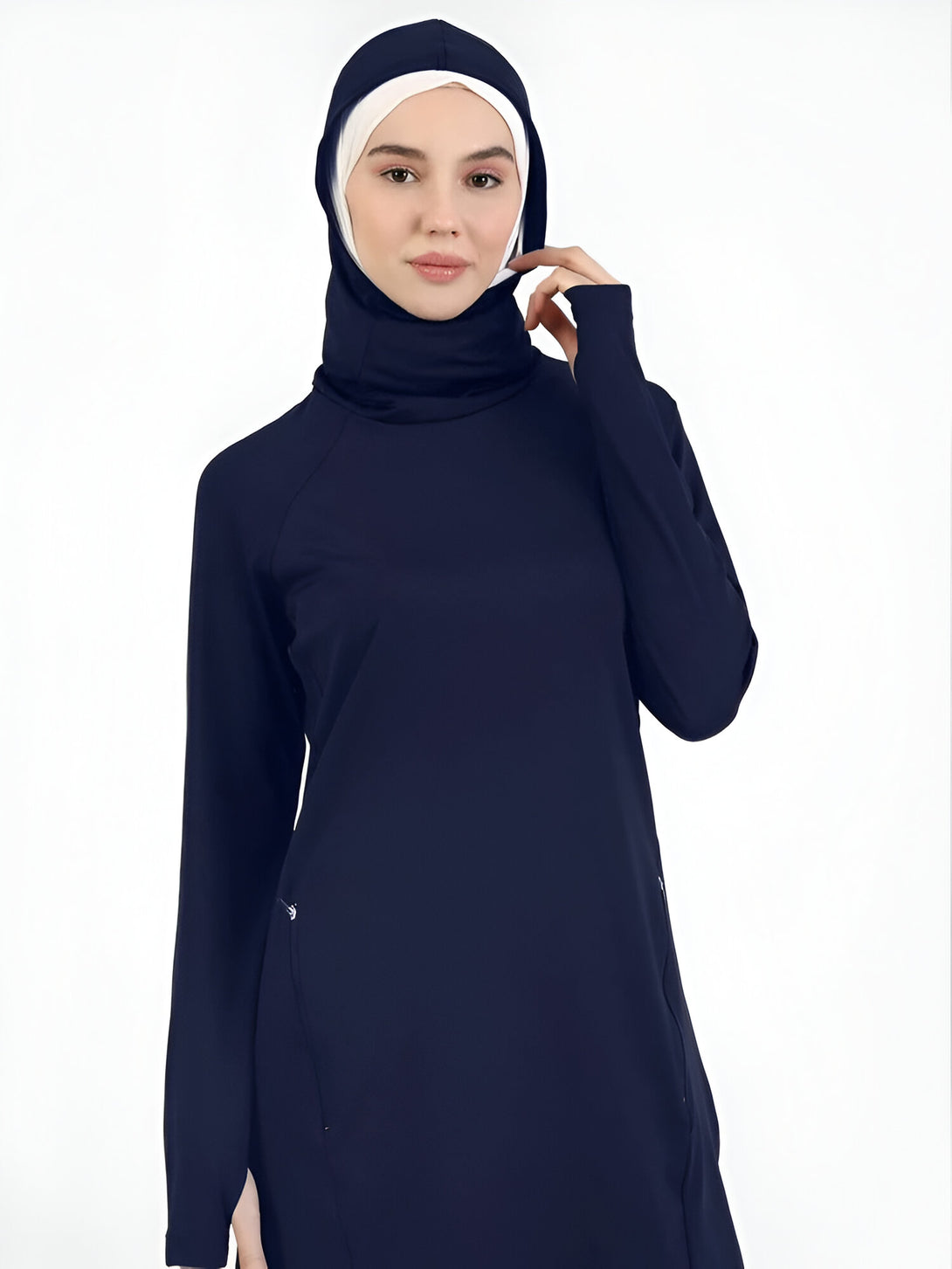 Une femme portant une robe longue bleue marine avec une capuche et des manches longues. La robe a des poches sur les côtés. La femme porte un hijab blanc sous la capuche.