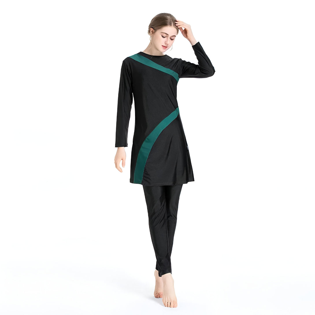 Une femme portant un maillot de bain musulman noir avec des détails verts. Le maillot de bain a des manches longues et des leggings. La femme a l'air confiante et à l'aise.